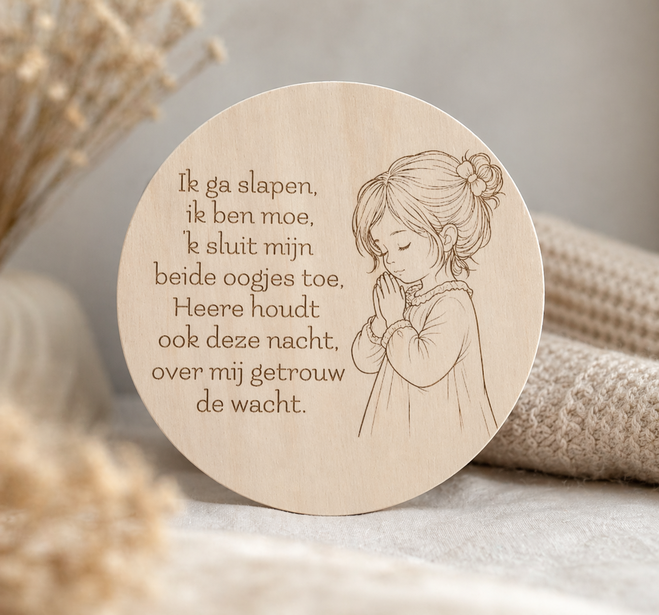 Ronde houten wanddecoratie met een gegraveerd kindergebed in het Nederlands en een fijne lijntekening van een biddend meisje, sfeervol gefotografeerd op een zachte, neutrale achtergrond met warme beige tinten en een rustige, huiselijke uitstraling.