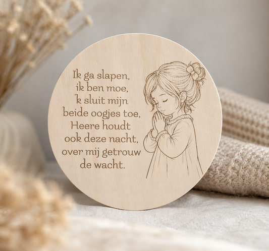 Ronde houten wanddecoratie met een gegraveerd kindergebed in het Nederlands en een fijne lijntekening van een biddend meisje, sfeervol gefotografeerd op een zachte, neutrale achtergrond met warme beige tinten en een rustige, huiselijke uitstraling.