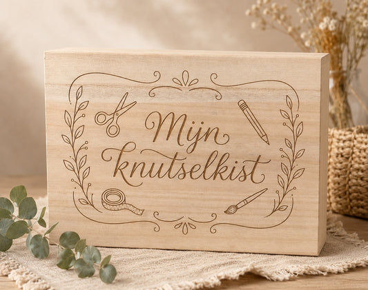 Houten knutselkist met de tekst: Mijn knutselkist. De tekst is in het hout gegraveerd. Om de tekst staan illustraties van een kwast, rolletje tape, schaar en een potlood. 
